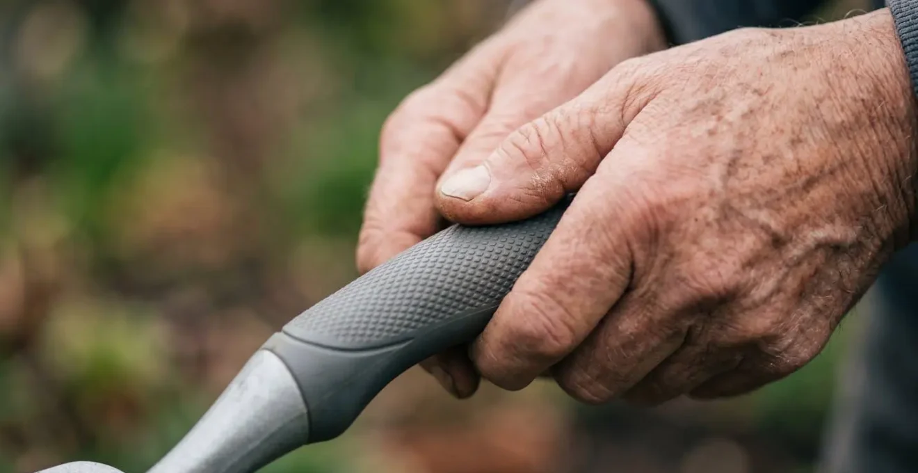 Mains de senior utilisant des outils de jardinage ergonomiques adaptés, symbolisant l'adaptation des loisirs