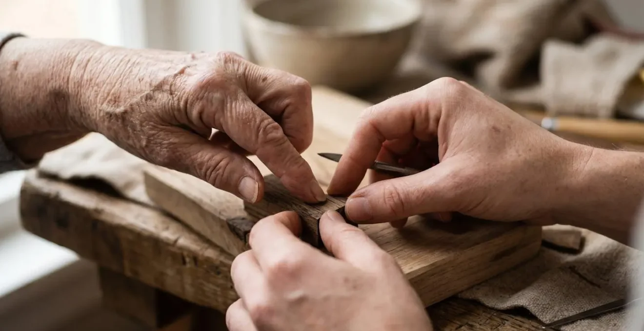 Gros plan sur les mains d'un senior guidant celles d'un jeune adulte dans un atelier créatif