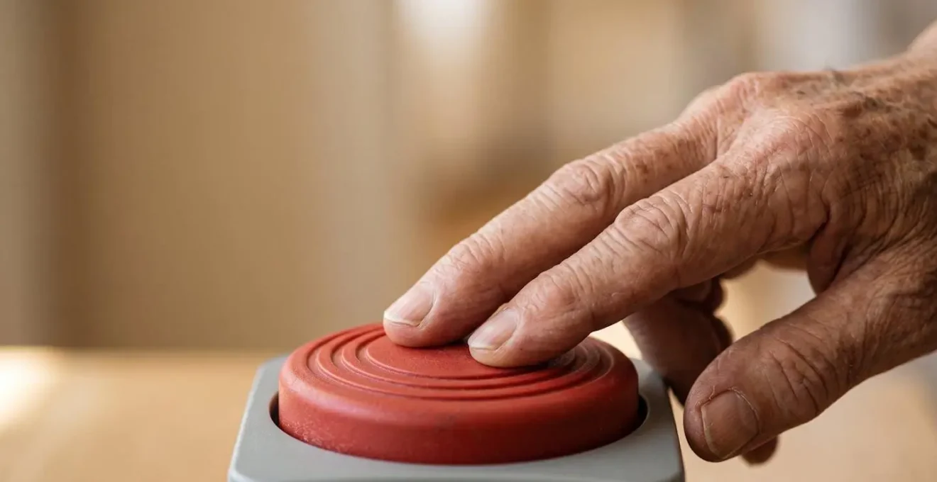 Gros plan sur une main de senior testant la simplicité d'un grand bouton d'alerte facile à manipuler