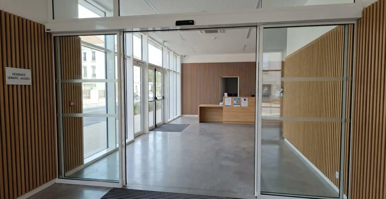Hall d'entrée moderne d'une résidence pour seniors avec portes automatiques et grande baie vitrée